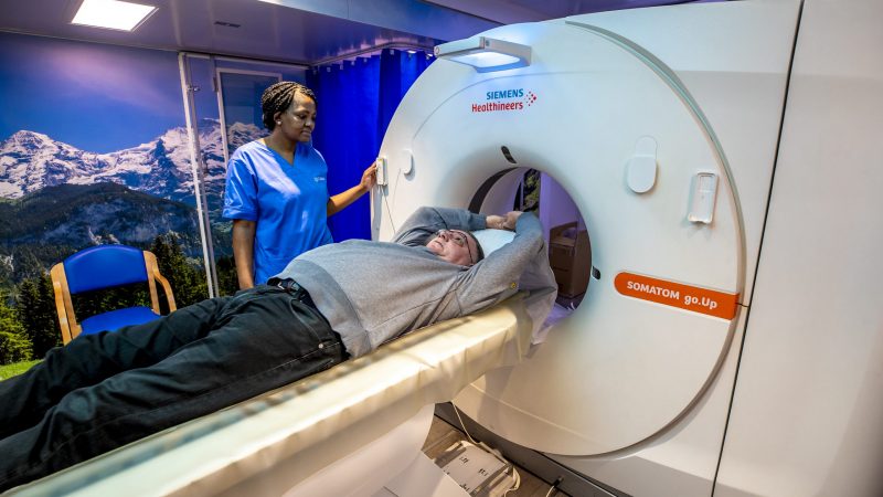 Gentleman laying in a CT scanner with nurse looking on
