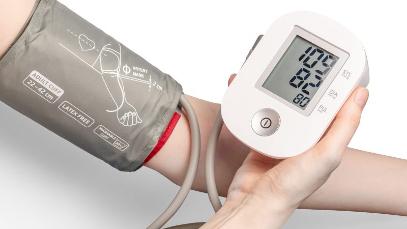 Blood pressure cuff around a persons arm with them holding the monitor in the other hand