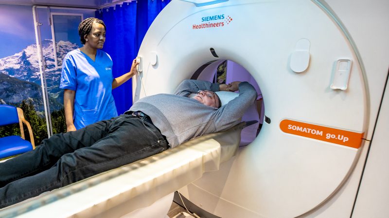 Man laying inside a CT scanner having a lung health check with a nurse looking on