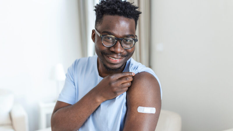 Covid-19 Vaccination. Portrait Of Happy Vaccinated African Man Showing His Arm After Coronavirus Antiviral Vaccine Shot . Covid Immunization Campaign Concept.