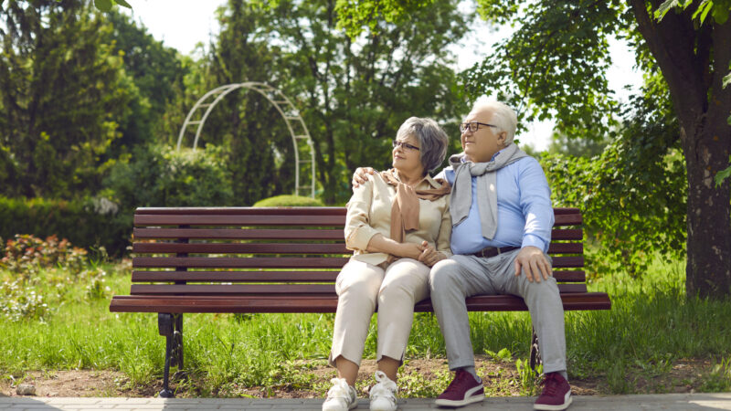 Happy elderly people couple sit on bench in park look in good maturity future dreaming together. Smiling mature man and woman spouses relax rest outdoors on weekend. Old life happiness.