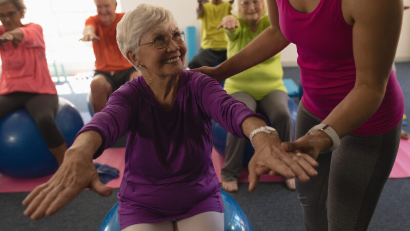 Female trainer assisting senior woman in fitness studio
