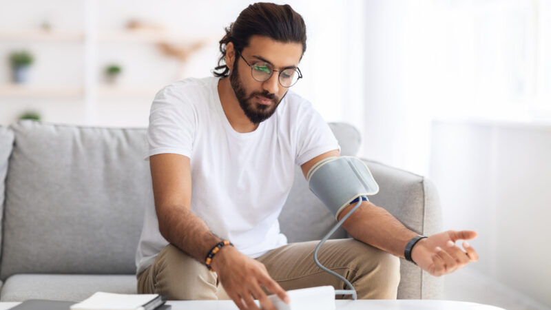 Young,Arab,Man,Sitting,On,Couch,,Checking,Blood,Pressure,And