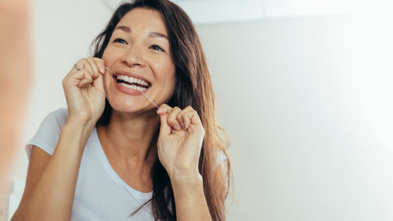 Woman,Looking,In,The,Bathroom,Mirror,And,Using,Dental,Floss